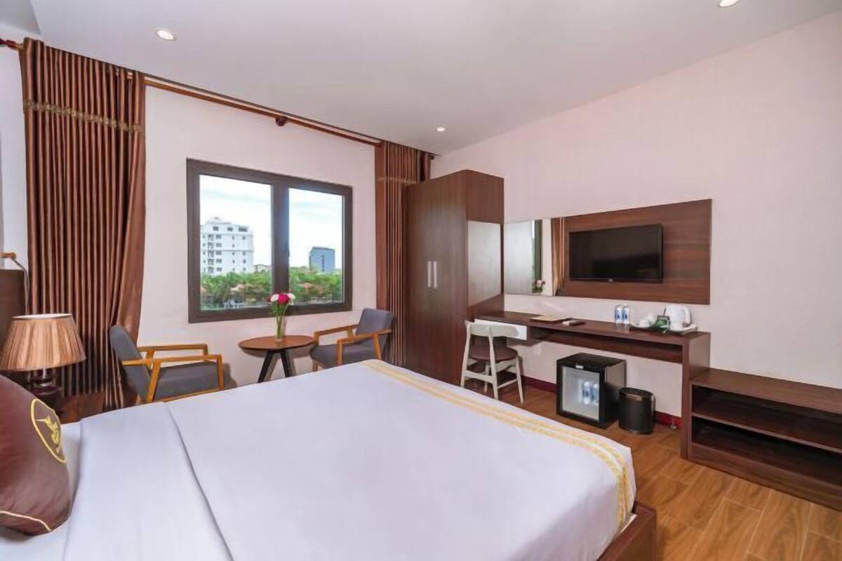 A hotel room with a bed, desk, TV, and a window with a city view.