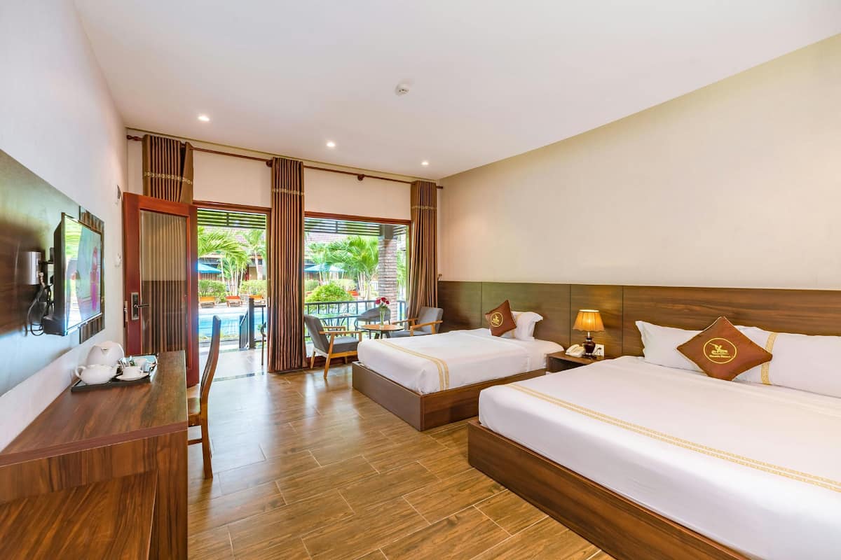 A hotel room with two beds, a wooden desk, a TV, and a balcony with a pool view.