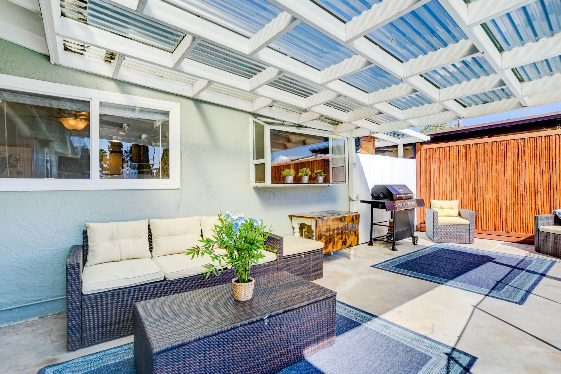 Ein Garten-Sitzbereich mit Rattan-Sofa, Grill und Holzlattenzaun.