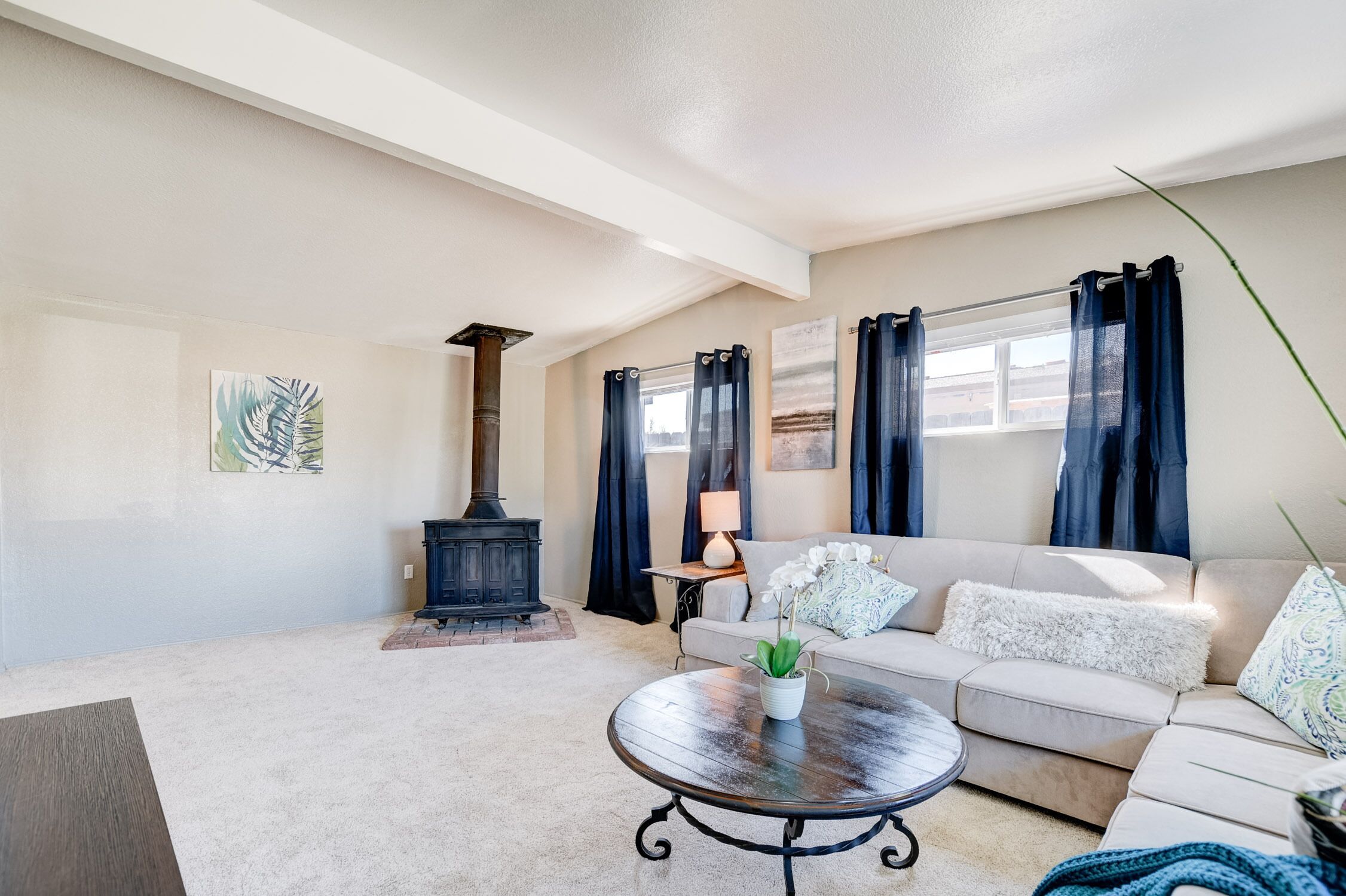 A cozy living room with a beige sofa, a round coffee table, a fireplace, and a window with curtains.