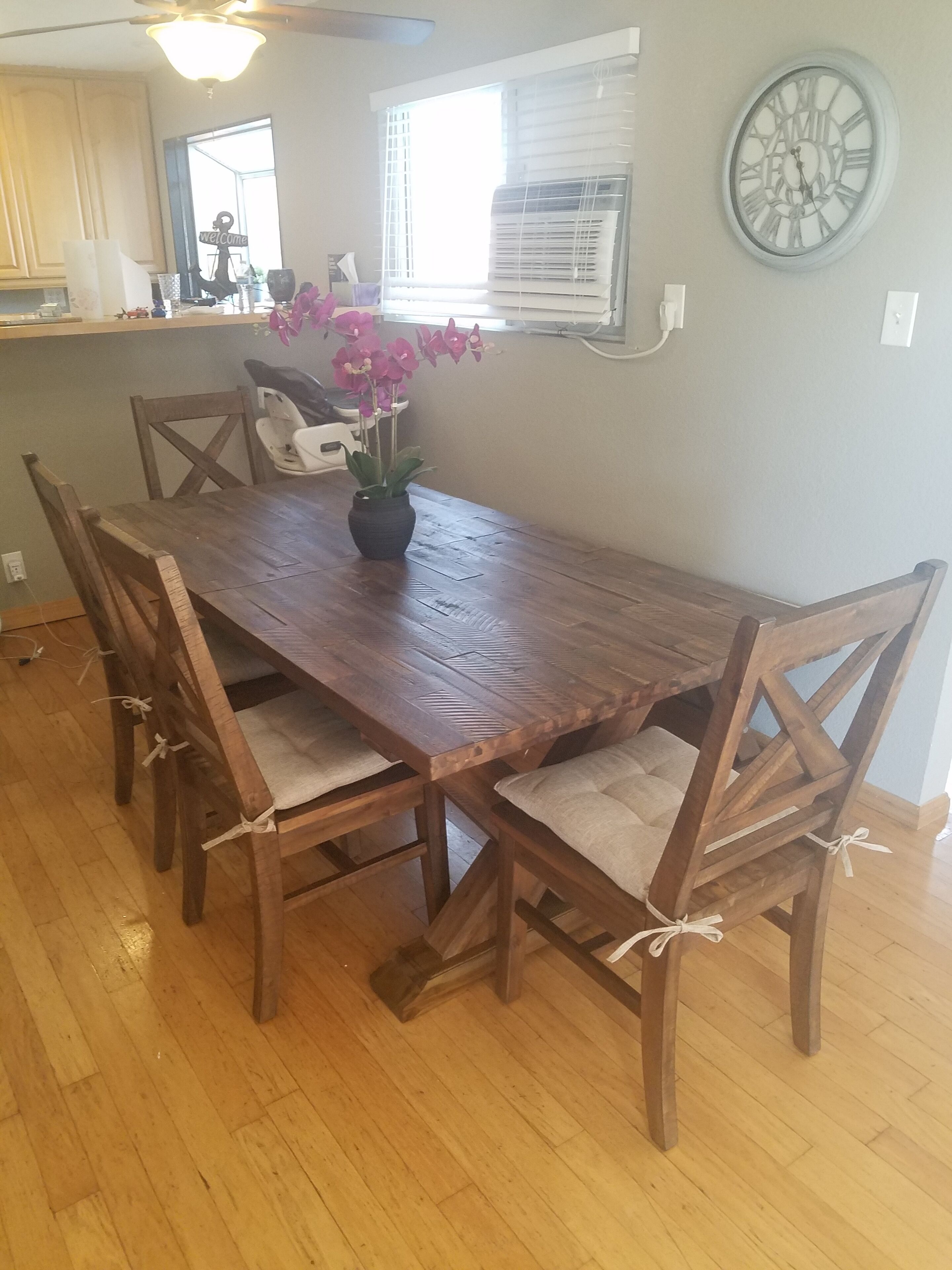A wooden dining table with cushioned chairs, a vase with flowers, and a wall clock.