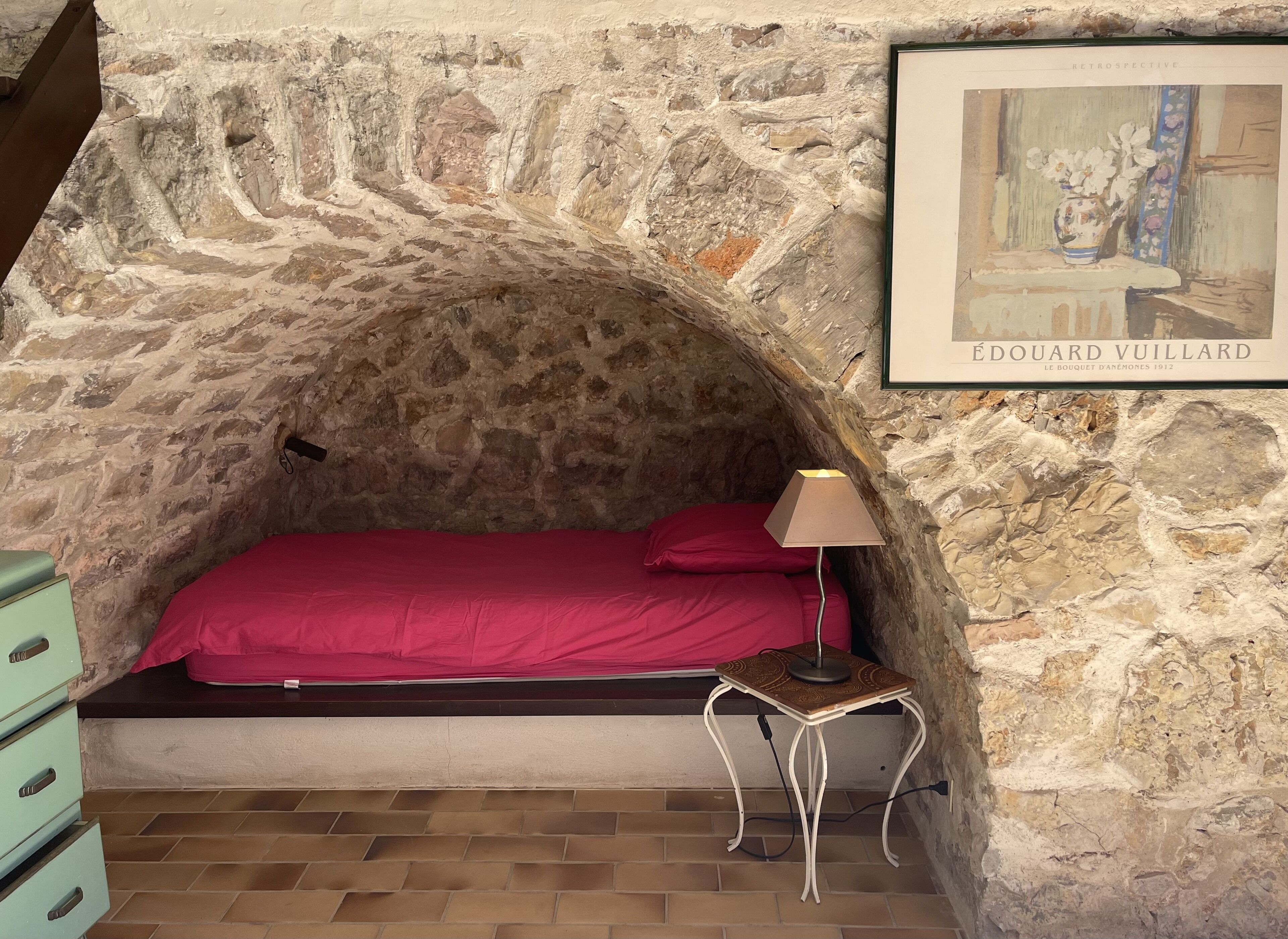 Un dormitorio con paredes de piedra, una cama, una mesita de noche y una obra de arte enmarcada.