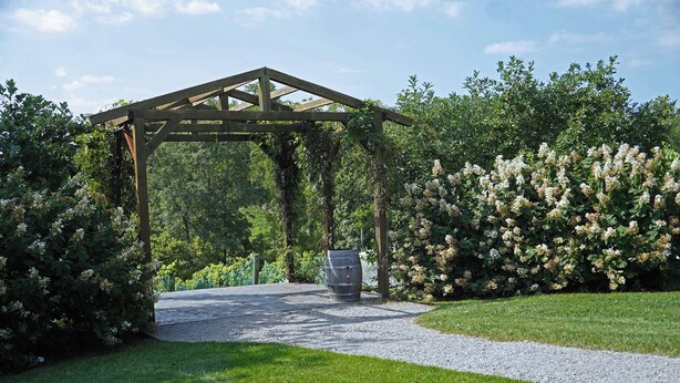 A wooden pergola structure in a garden with a gravel path leading to it.
