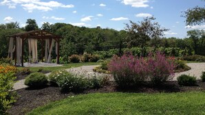 A gazebo with a pergola structure, surrounded by a garden with various plants and flowers.
