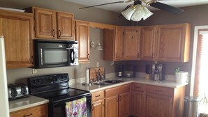 A kitchen with wooden cabinets, a black stove, a microwave, a sink, and a ceiling fan.