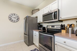 A kitchen with white cabinets, stainless steel appliances, a clock, and a coffee maker.