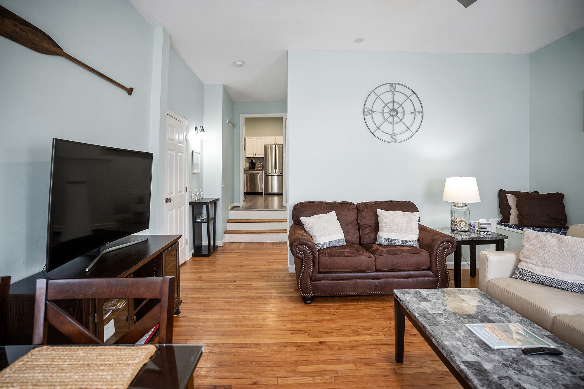 A living room with a television, leather sofa, coffee table, and a dining area with a chandelier.