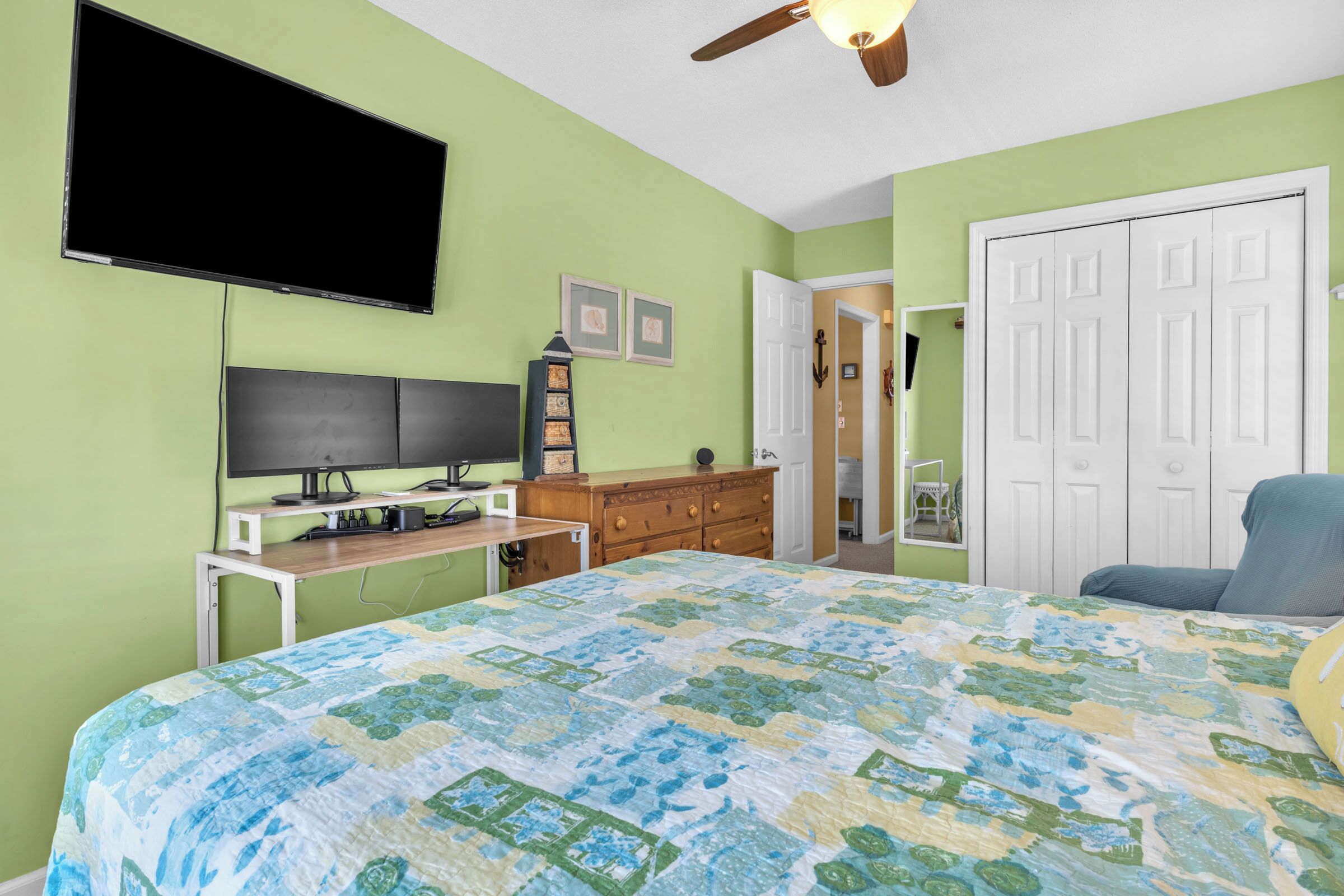 A bedroom with a bed, a desk, a television, a wardrobe, and a ceiling fan.