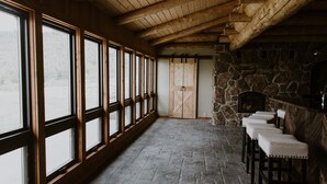 Una habitación con ventanas amplias, suelo de piedra, vigas de madera y chimenea de piedra.