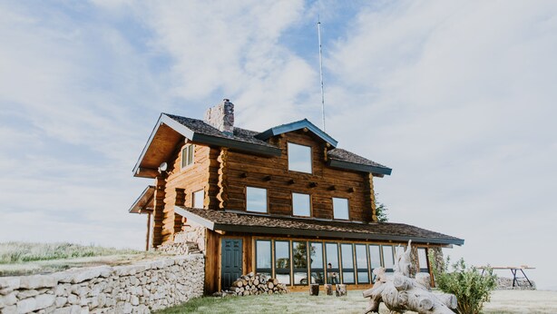 Una cabaña de troncos con cimientos de piedra, ventanas amplias y una chimenea.