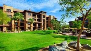 A hotel with a well-maintained lawn, outdoor seating area, and multiple buildings with balconies.