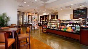 A café with wooden tables and chairs, a refrigerated display case with beverages, and a chalkboard menu.
