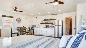 Une chambre d’hôtel compacte comprenant un lit, une table à manger avec des chaises, un coin cuisine et un ventilateur de plafond.