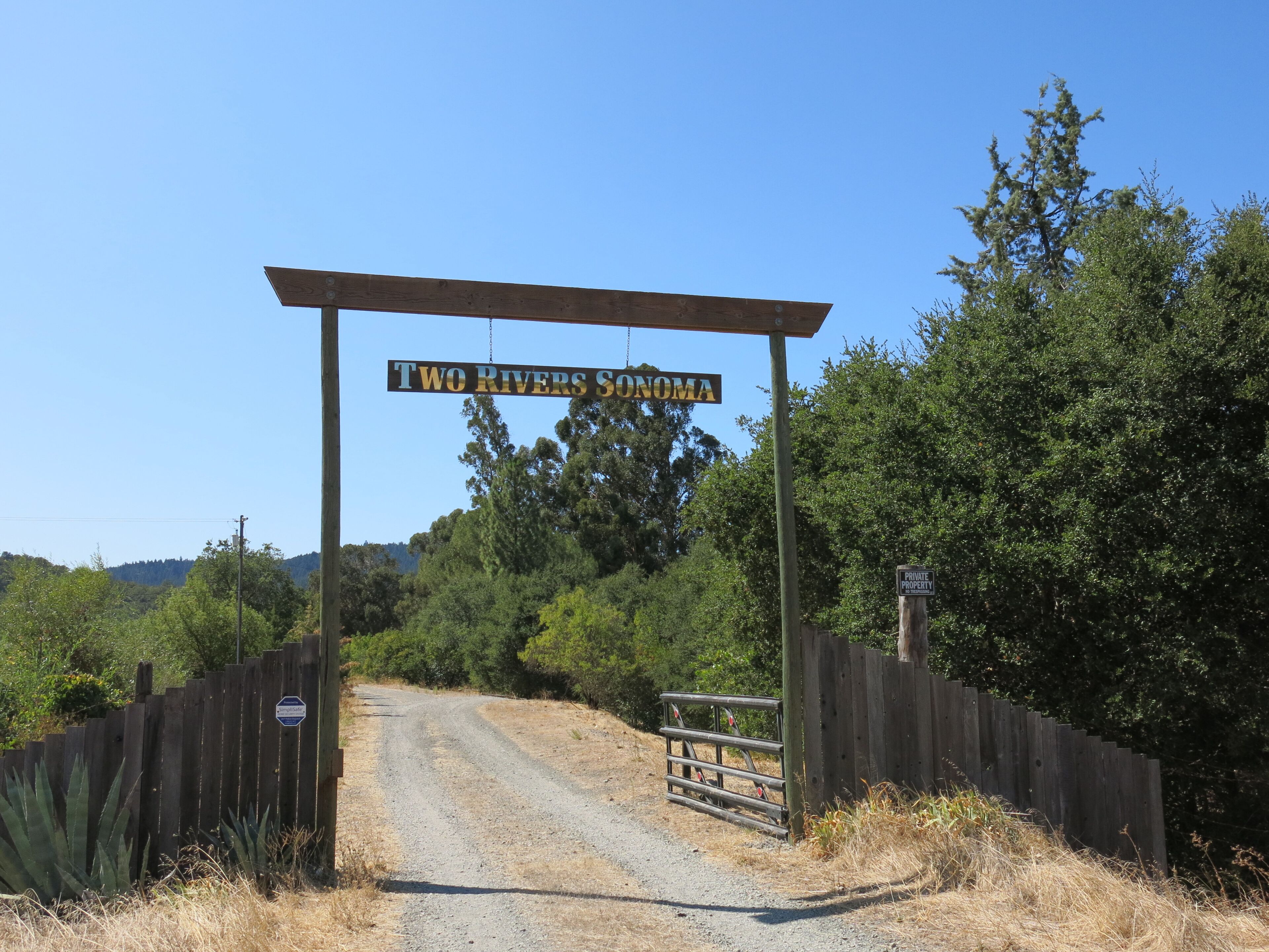 A rural entrance with a wooden gate and a sign reading "Two Rivers Sonoma".