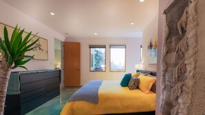 A bedroom with a bed, a dresser, a plant, and a window.