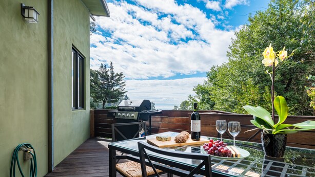 An outdoor patio with a table set for a meal, a grill, and a view of the sky.