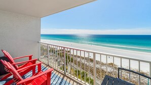 Ein Balkon mit Blick auf einen Strand, roten Stühlen und einem Geländer.