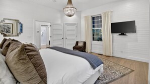 A bedroom with a large bed, a chandelier, a television, and a door leading to another room. - Blue Ridge- Hot Tub - EV Outlet -Outdoor Oasis (Blue Ridge)