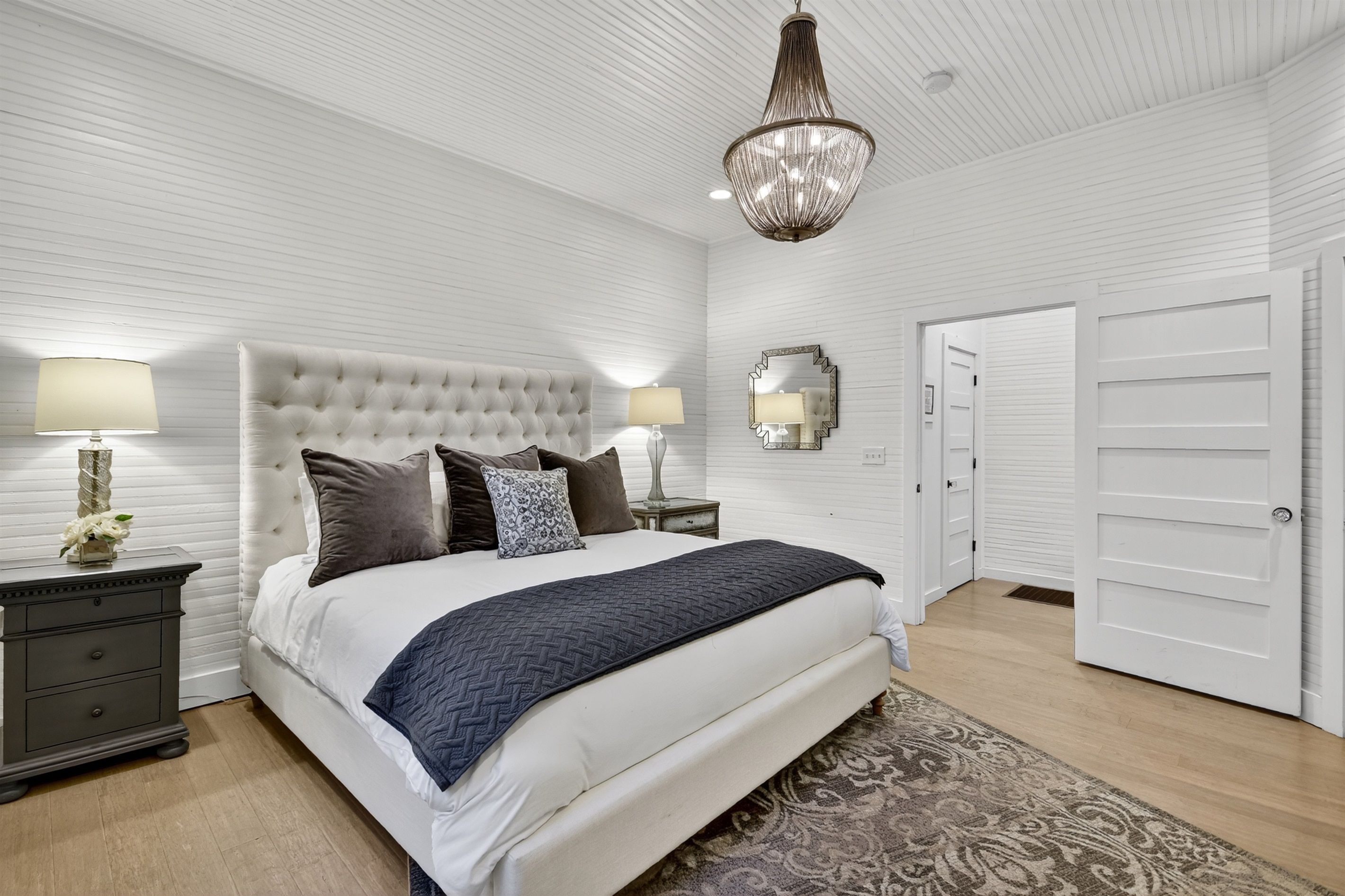 A bedroom with a tufted headboard, two bedside tables with lamps, a large mirror, and a wardrobe.