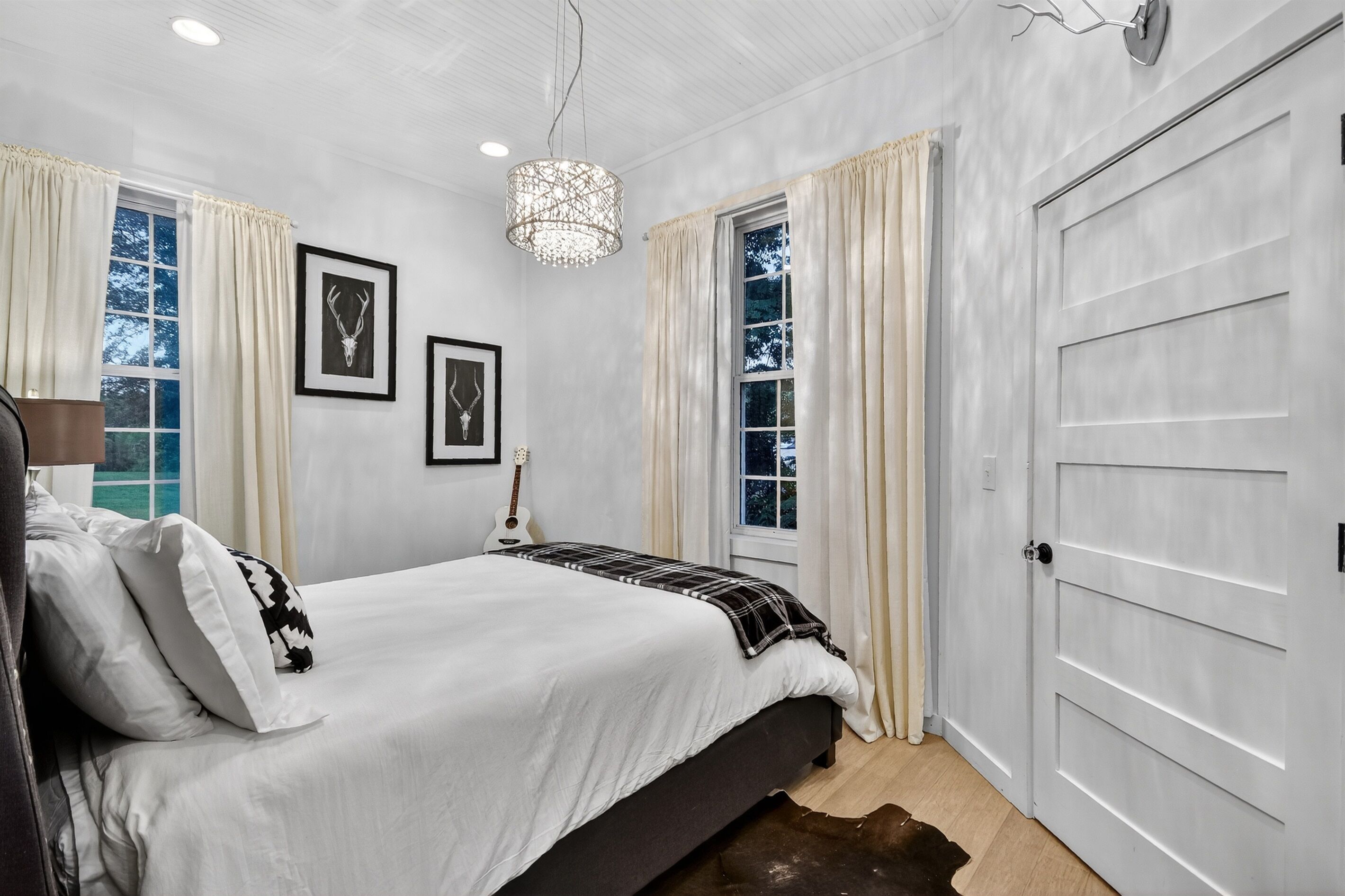 Quarto com cama, quadros nas paredes, um violão e uma porta.
