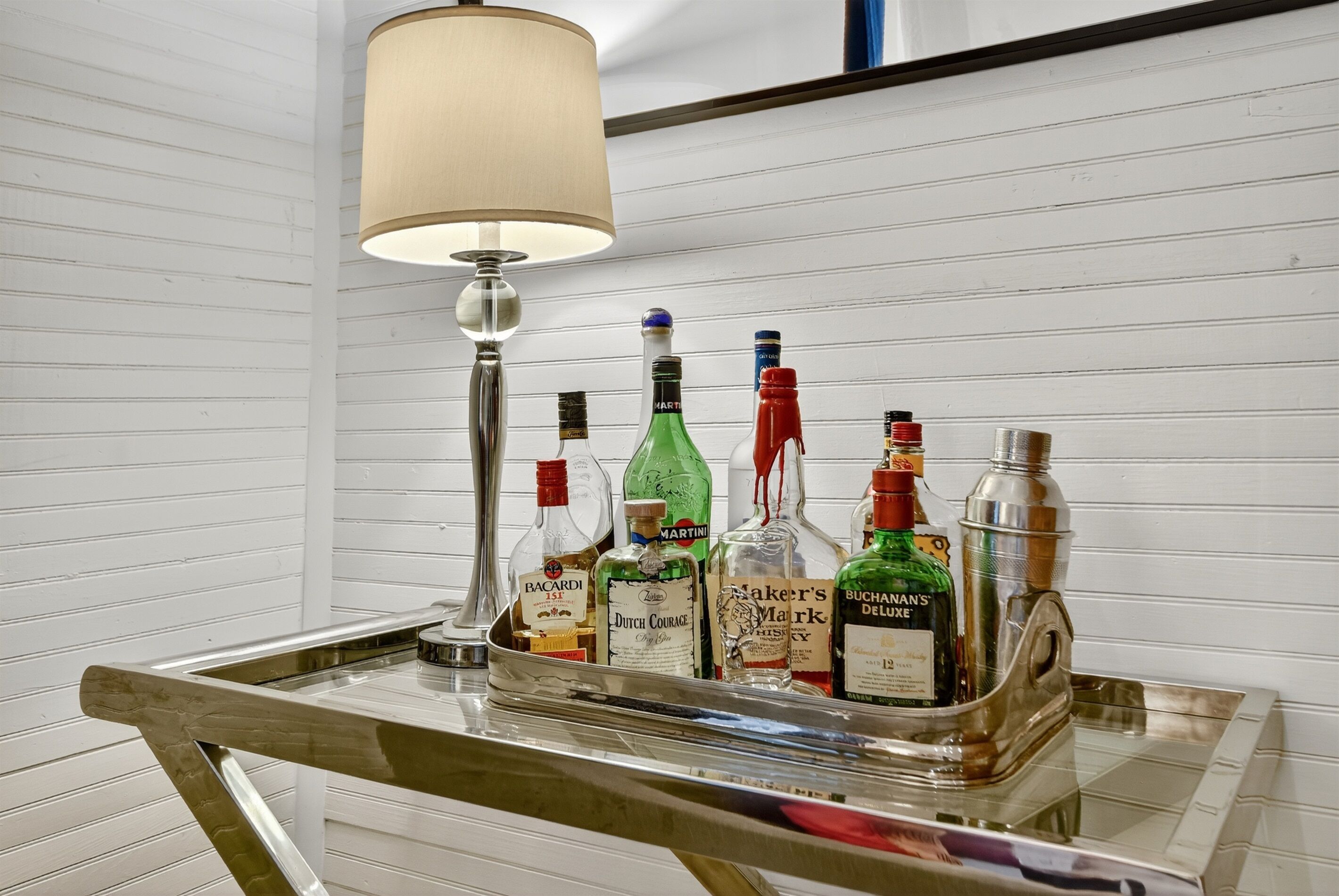 Un coin bar avec un plateau rempli de bouteilles d’alcool, une lampe et un miroir.
