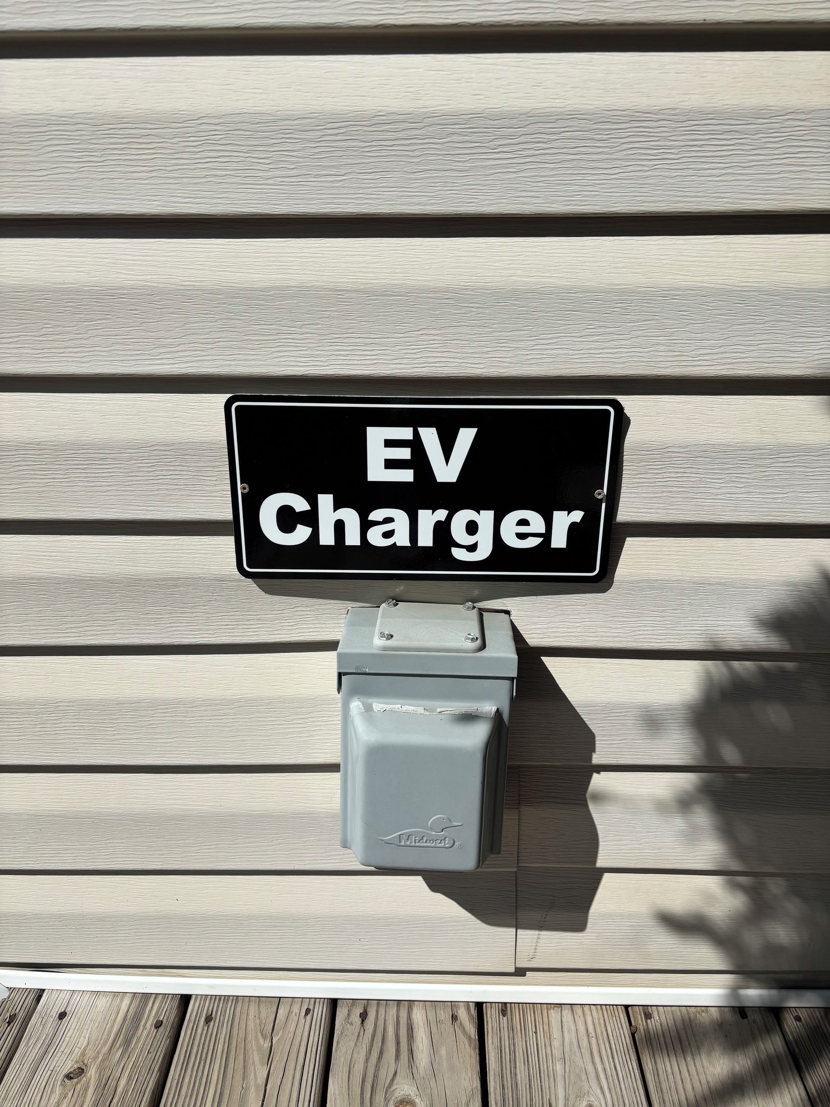 A sign for an EV Charger mounted on a wooden surface.