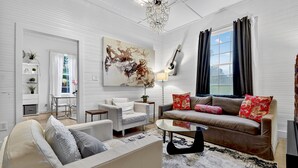 A modern living room with a beige sofa, a brown sofa with red cushions, a white armchair, and a glass coffee table. There is a large abstract painting on the wall, a chandelier, and a guitar leaning against the wall. - Blue Ridge- Hot Tub - EV Outlet -Outdoor Oasis (Blue Ridge)