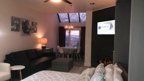 Une chambre d’hôtel moderne équipée d’un lit, d’un canapé, d’une table à manger avec des chaises, d’un lustre et d’un écran de télévision affichant un site web.