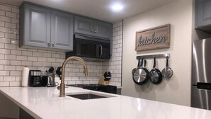 Une cuisine moderne avec des meubles gris, un réfrigérateur en acier inoxydable, un plan de travail blanc et un porte-casseroles fixé au mur.