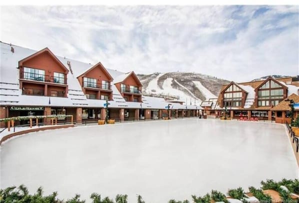 A ski resort with multiple chalet-style buildings, a large open plaza, and a mountain backdrop.