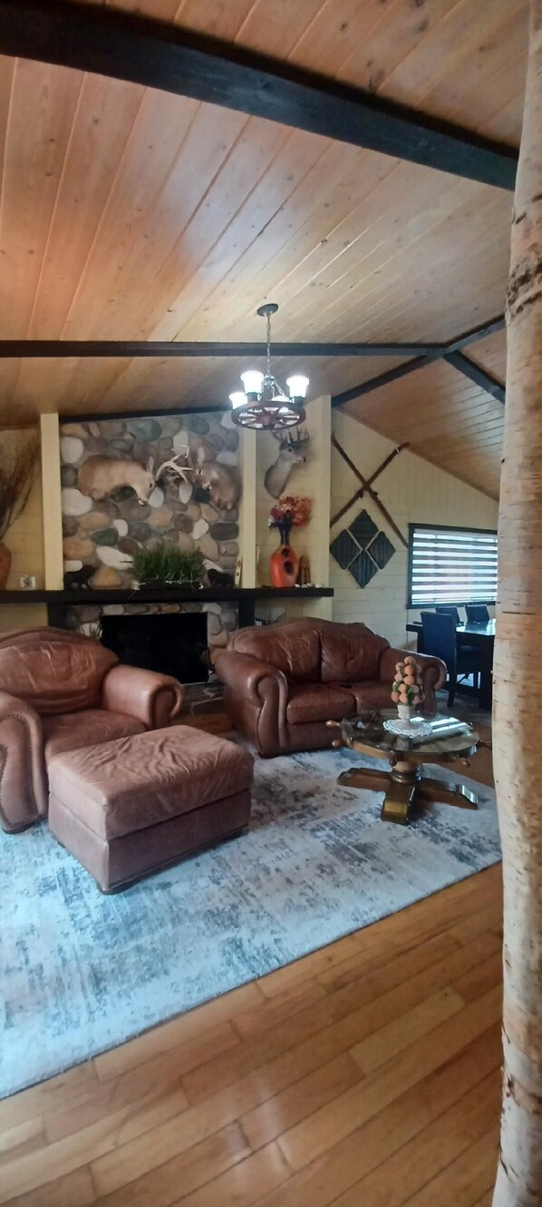 Uma sala de estar aconchegante com lareira de pedra, sofás de couro e um candelabro.