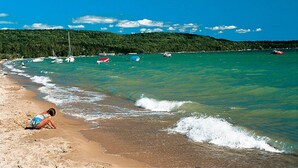 Una playa con agua turquesa cristalina, barcos y una persona en la arena.