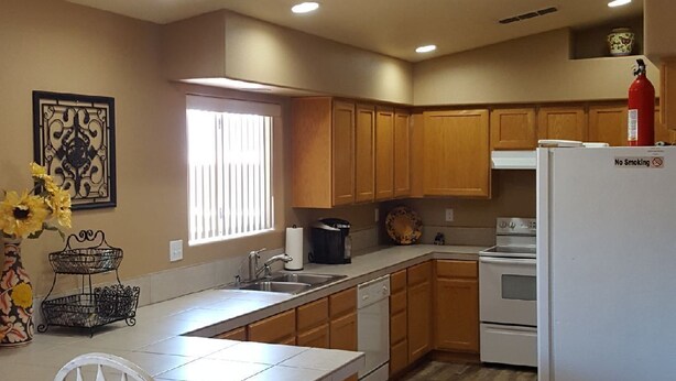 A kitchen with wooden cabinets, a white refrigerator, a stainless steel trash can, and a window with blinds. - snowbirds email of call for winter pricing<br>951-741-7590 occapt@hotmail.com (Lake Havasu City)