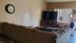 A living room with a sectional sofa, a flat-screen TV, a small table, and a fan. - snowbirds email of call for winter pricing<br>951-741-7590 occapt@hotmail.com (Lake Havasu City)