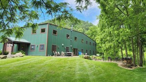 A green metal building with a covered outdoor seating area and a grassy lawn. - MCR  is a property that features seclusion and privacy that is hard to find.  (Rushford)