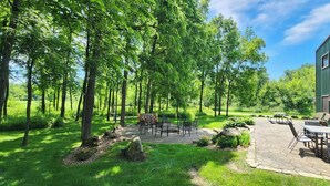 A patio area with outdoor seating and a fire pit, surrounded by lush greenery and trees. - MCR  is a property that features seclusion and privacy that is hard to find.  (Rushford)