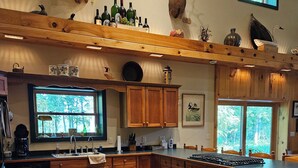 A spacious kitchen with wooden cabinets, a large island, and a rustic decor including mounted animal heads and a variety of bottles. - MCR  is a property that features seclusion and privacy that is hard to find.  (Rushford)