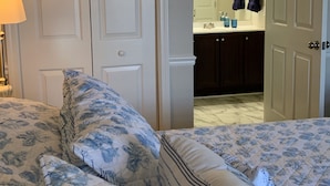 Une chambre avec deux lits, une salle de bain visible à travers une porte ouverte et une table de chevet avec une lampe.