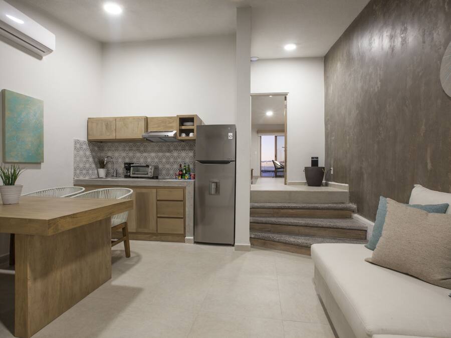 A modern kitchen with wooden cabinets, a stainless steel refrigerator, and a dining area with a wooden table and chairs.