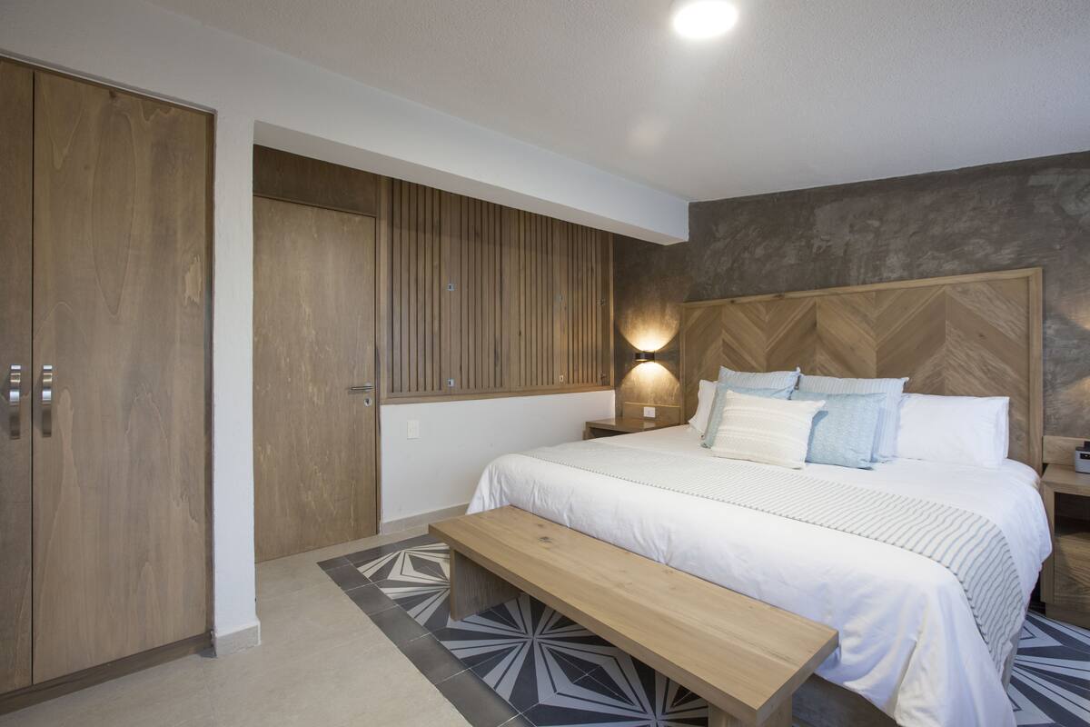 A bedroom with a large bed, a wooden bench, a nightstand with a lamp, and a wardrobe.