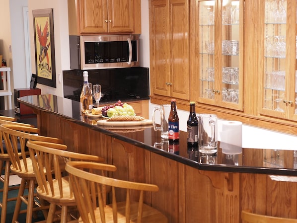 A kitchen with wooden cabinets, a stainless steel microwave, and a bar area with chairs and a counter displaying food and drinks. - Quiet Country Setting (Gettysburg)