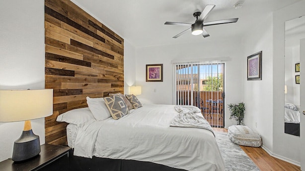A bedroom with a wooden headboard, a bed with white bedding, a ceiling fan, and a view of a balcony. - Dessert Oasis - 2BR Desert Breeze Retreat with Pool - jacuzzi- Gym (Phoenix)