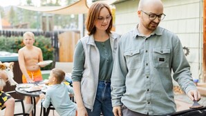 Une famille est réunie autour d’une table et de chaises en plein air, près d’un barbecue, avec une piscine en arrière-plan.