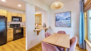 Une cuisine moderne avec des meubles en bois, un réfrigérateur noir, un four à micro-ondes et une cuisinière. On y trouve également un coin repas avec une table en bois et des chaises roses.