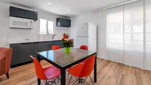 A modern kitchen with a dining area, featuring a glass-top table, red chairs, and a green vase with flowers. - Oceanviews, Steps to the Sand, Short Walk to the Village! A/C (Carlsbad)