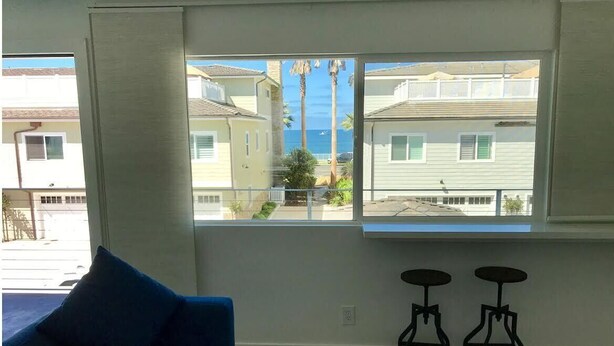 A room with a large window, a blue sofa, and two black stools. - Oceanviews, Steps to the Sand, Short Walk to the Village! A/C (Carlsbad)