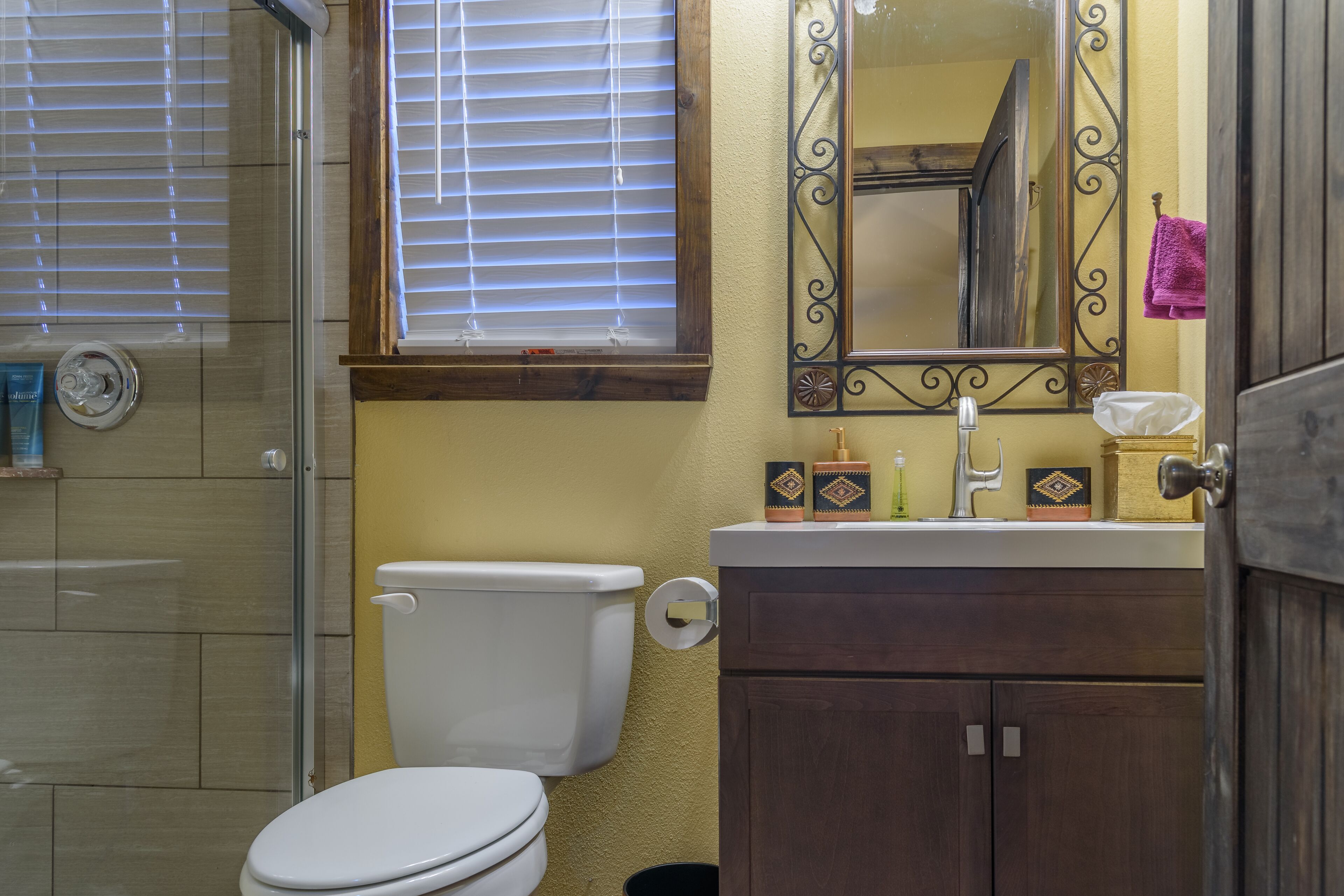 A bathroom with a toilet, a shower, a sink with a mirror, and a towel hanging on a rack.