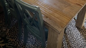 Una mesa de comedor de madera con seis sillas, una planta en maceta y un juego de copas de vino sobre un atril.