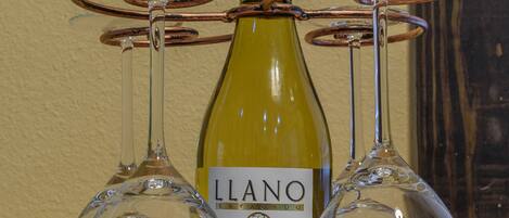 A bottle of Llano Estate Chardonnay Blanc on a wooden board with four wine glasses.