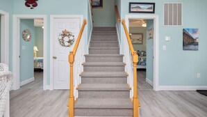 Una escalera con barandilla de madera, peldaños alfombrados y una pared azul claro con una puerta en la parte superior.